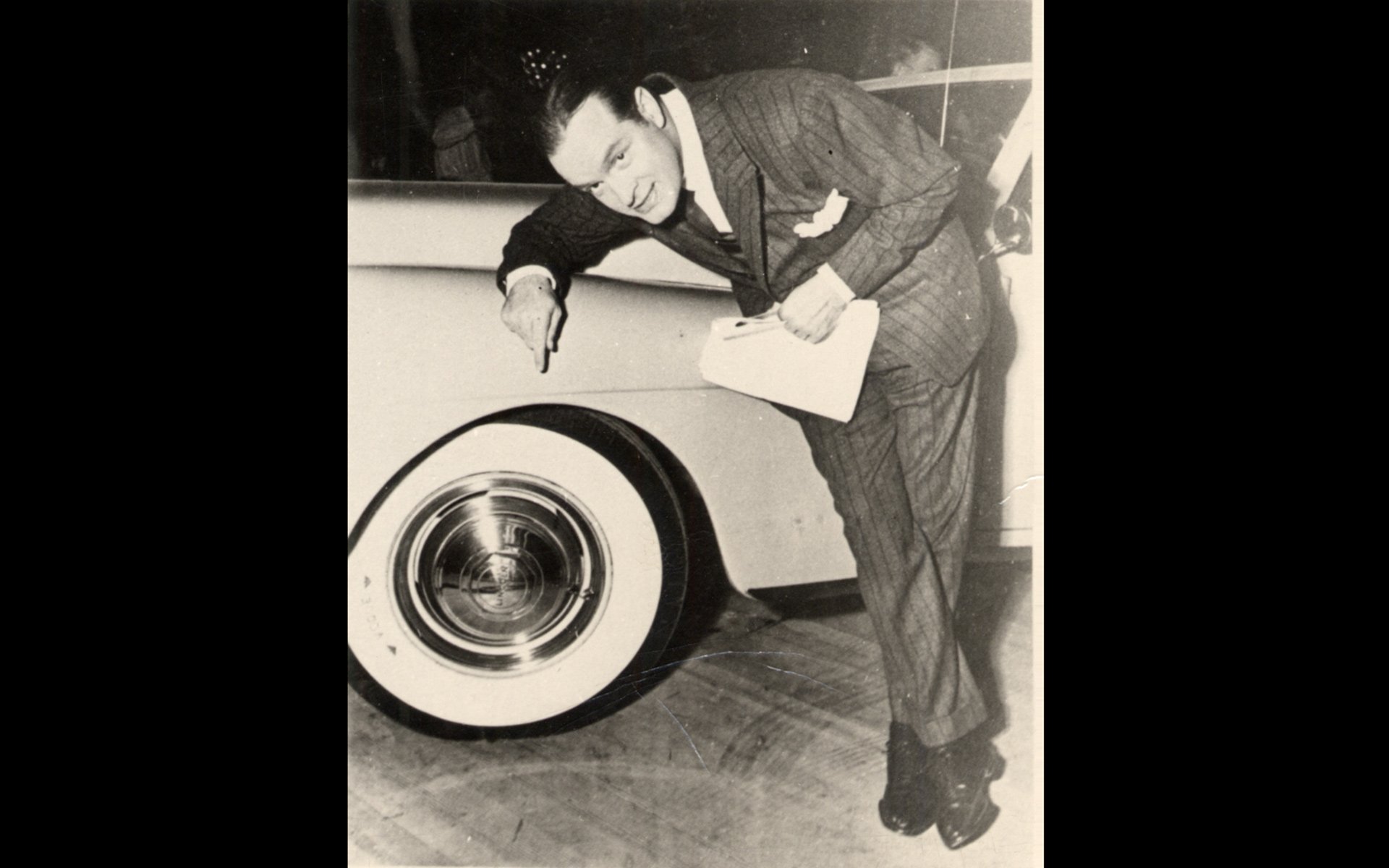 Bob Hope pointing to Vogue Tyre whitewall tires on a vehicle.